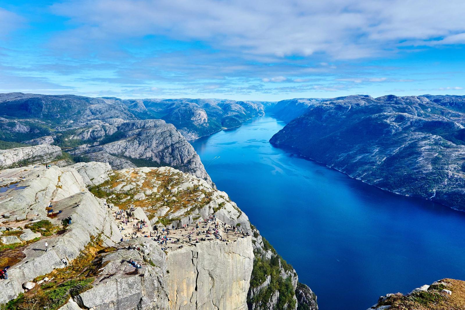A deep blue fjord between steep granite cliffs, seen from a high rocky ledge
